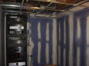 The drop ceiling goes in and drywall is being prepped for paint near the media cabinet